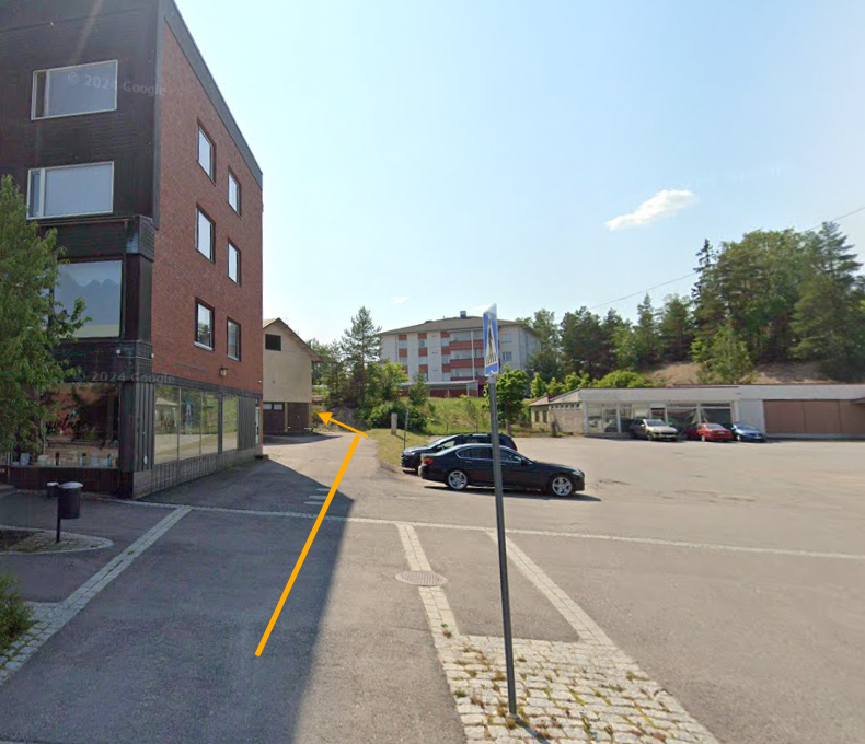 Näin saavut toimitilaani. Toimitilaan tuova ulko-ovi löytyy takana olevan vaalean rakennuksen takaa. Ovestä kuljettuasi saavut pieneen rappukäytävään, jossa ovessa on selkeä nimikyltti.